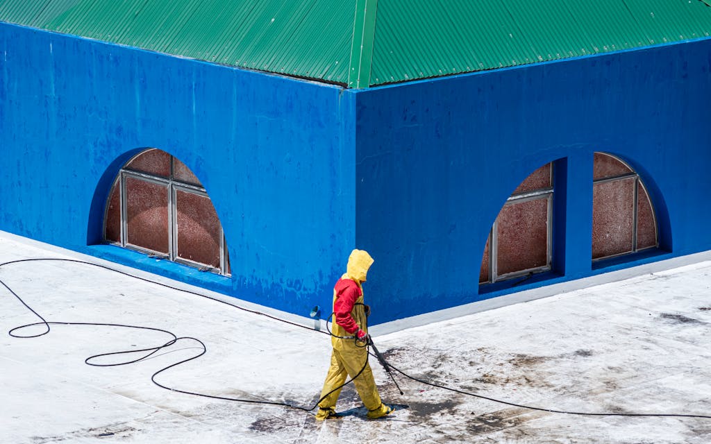 A worker in protective gear power washes a vibrant blue building exterior.