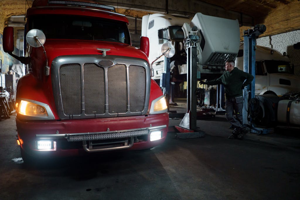 Red truck in a garage with mechanic and elevated vehicles undergoing maintenance.