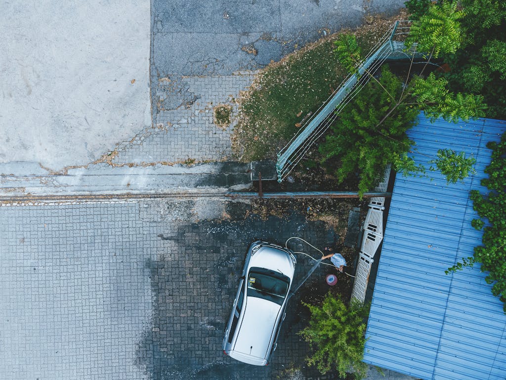 Top-down drone shot of a person washing a car in Ipoh, amidst urban and green surroundings.