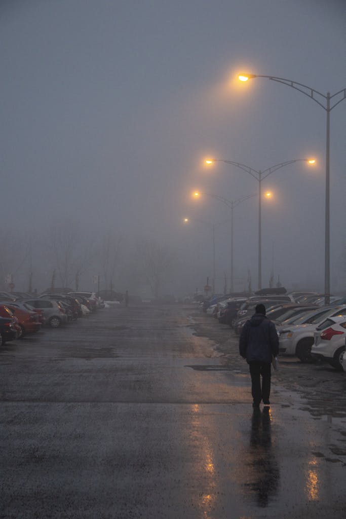 A lone figure walks through a foggy parking lot in Québec at night.